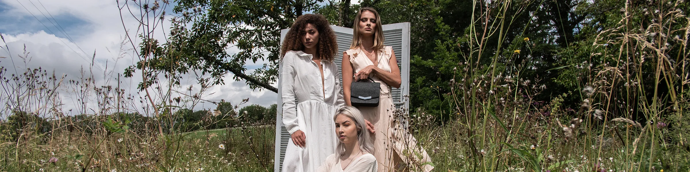 Bannière Allure Sauvage : trois femmes dans un champ de hautes herbes, l’une tenant un sac noir en Piñatex